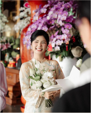 Cô dâu mỉm cười cầm bó hoa trắng trước hoa tím