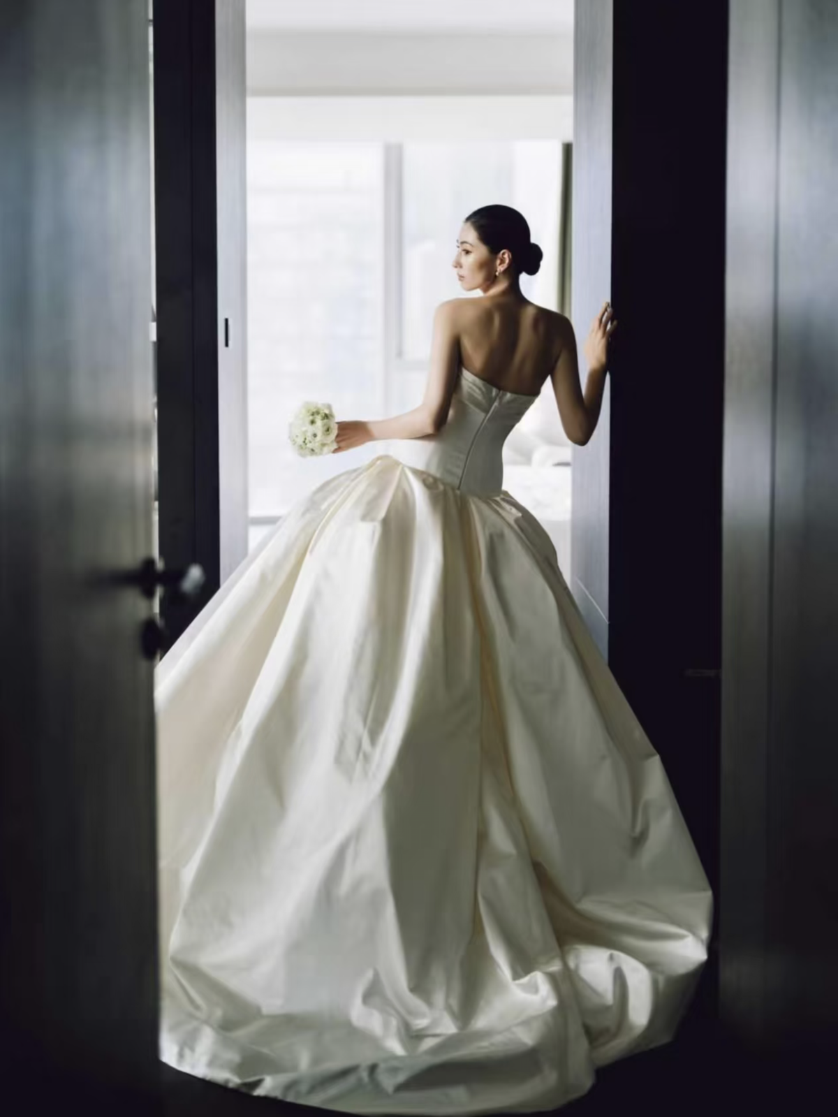 Góc lưng váy satin xòe, cô dâu đứng tại cửa sổ
