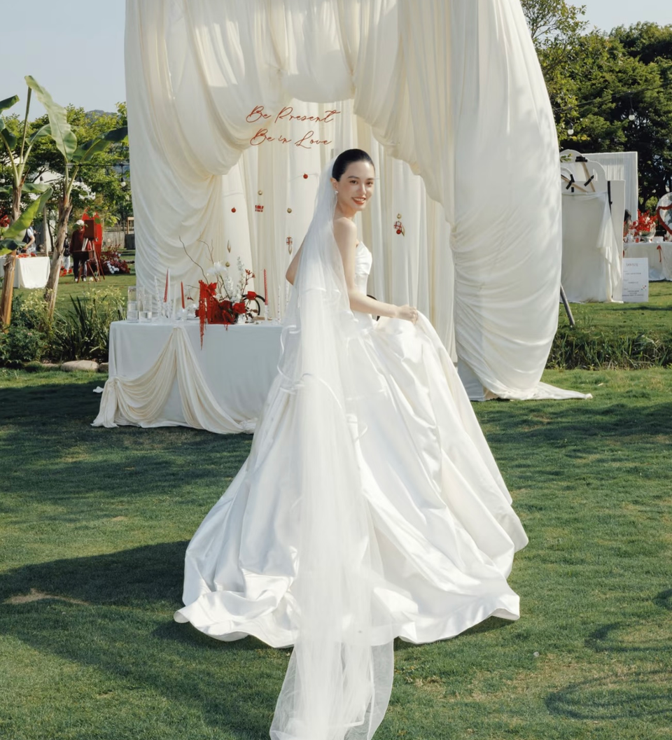 Cô dâu quay lại mỉm cười trên thảm cỏ trước phông rèm trắng
