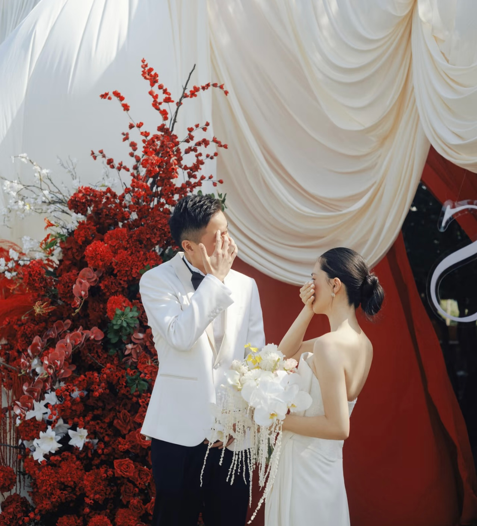 Cô dâu chú rể lau nước mắt trước rèm trắng và hoa đỏ