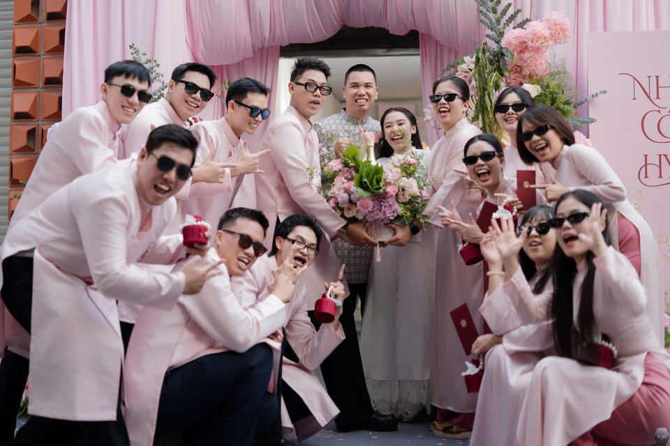 Cô dâu chú rể cùng bạn bè đeo kính râm trước phông hoa hồng