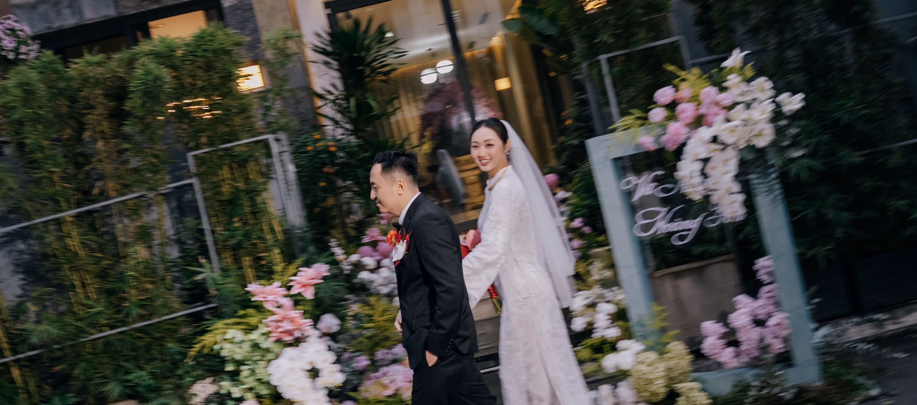 Cô dâu chú rể bước qua lối vào được trang trí bằng hoa hồng và cây xanh