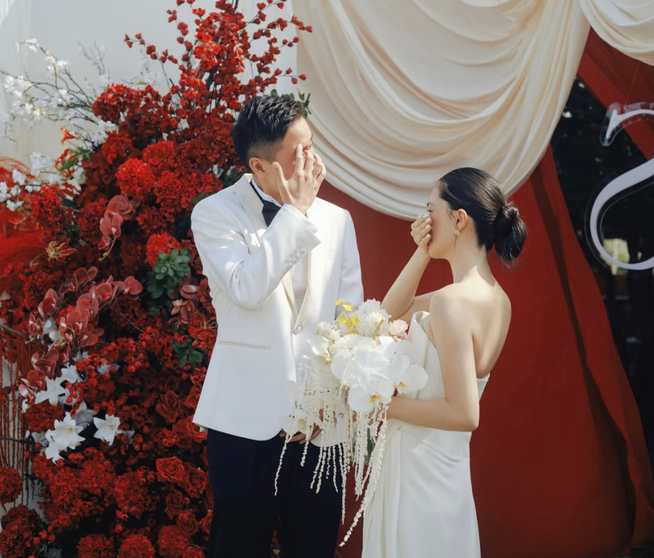 Chú rể xúc động bên cô dâu trước hoa đỏ và rèm kem